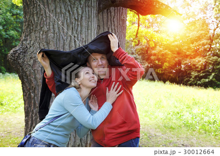 man and the woman near an oak hide from a rain in  30012664
