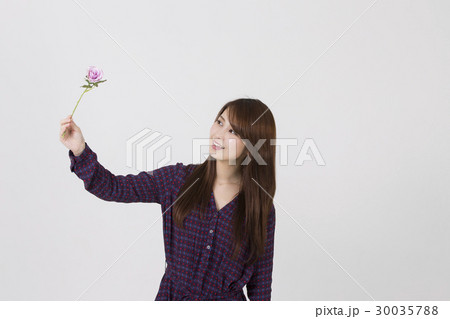 白い背景の前で右手で持っている花一輪を見ている若い女性の写真素材