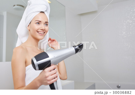 Young woman blow drying hair in bathroom Young woman blow drying hair in bathroom 30036882