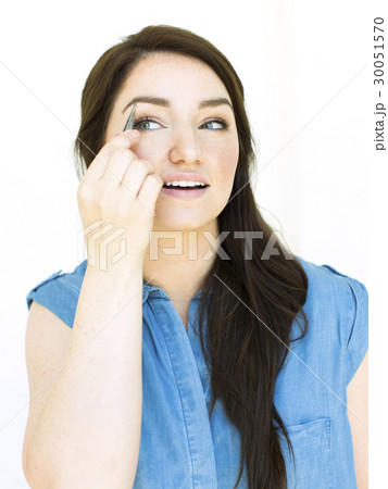 Woman wearing blue top tweezing eyebrow 30051570