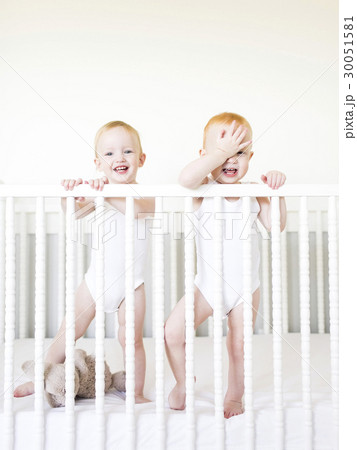 Twin brothers (12-17 months) standing in crib 30051581