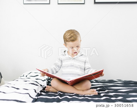 Boy (4-5) sitting on bed and reading book 30051658