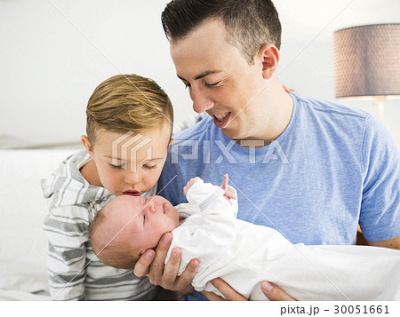 Father carrying daughter (0-1 months) and sitting on bed with son (4-5) 30051661