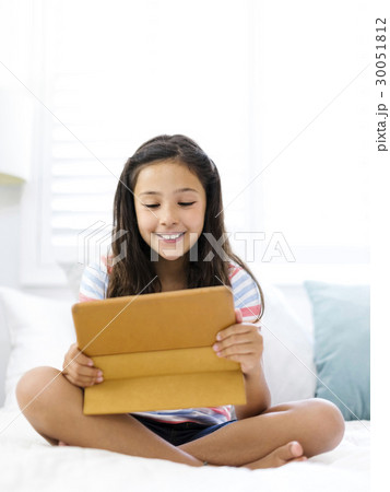 Smiling girl (10-11) sitting and watching tablet Smiling girl (10-11) sitting and watching tablet 30051812