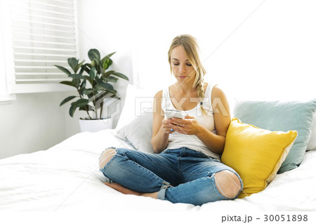 Young woman with mobile phone sitting on bed 30051898