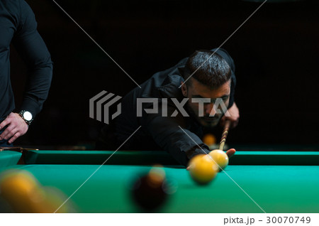 Young man playing billiard in dark club. 30070749
