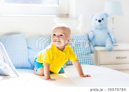 Baby boy playing on bed in sunny nursery Baby boy playing on bed in sunny nursery 30079789