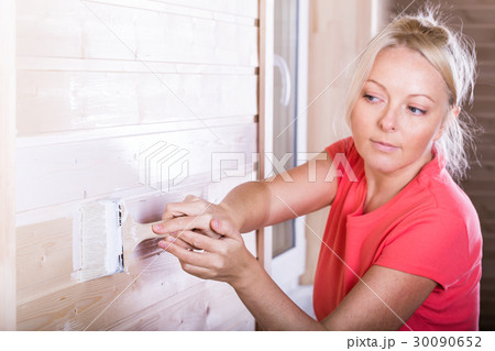 Woman painting wooden boards in white color 30090652