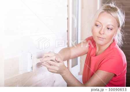 Woman painting wooden boards in white color 30090653
