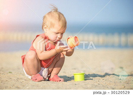 Baby girl in red dress playing on sandy beach near Baby girl in red dress playing on sandy beach near 30120529
