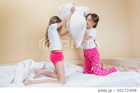 Two girls in pajamas fighting with pillows on bed 30172409
