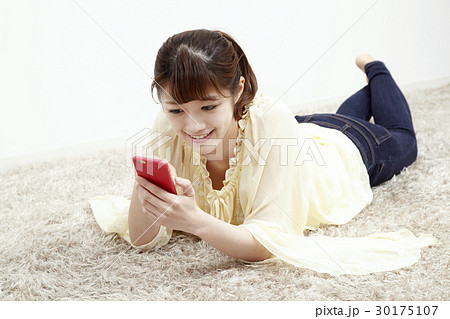 床に寝そべってスマホを触る若い女性 30175107