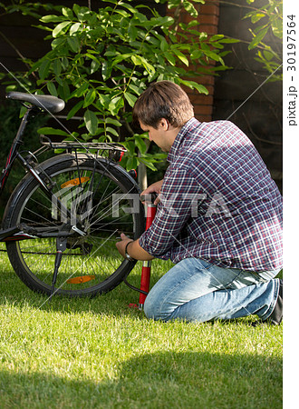 Young man pumping up bicycle tyre at park Young man pumping up bicycle tyre at park 30197564