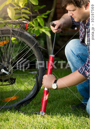 Young handsome man pumping bicycle tires at park Young handsome man pumping bicycle tires at park 30197569