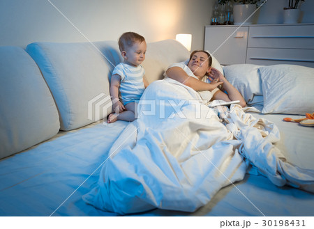 Sleepless baby waking up mother sleeping in bed Sleepless baby waking up mother sleeping in bed 30198431