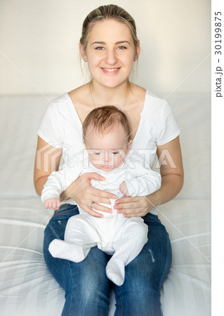 Smiling woman sitting at bedroom and holding baby Smiling woman sitting at bedroom and holding baby 30199875
