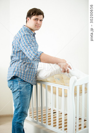 Father putting mattress in baby's cot at nursery 30200656