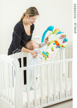 Young mother holding cute baby boy in wooden cot 30200669