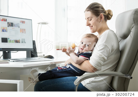 Beautiful woman feeding baby from bottle at work Beautiful woman feeding baby from bottle at work 30200724