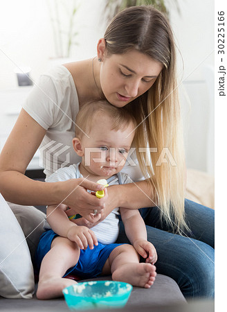 Mother sitting on sofa and feeding her baby Mother sitting on sofa and feeding her baby 30225166
