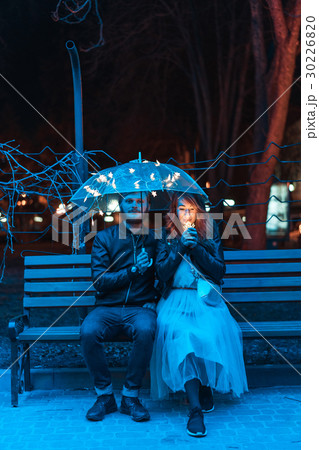 Guy and girl sitting on a bench under an umbrella 30226820