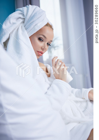 A woman in a bathrobe and a towel on her head lies on a bed A woman in a bathrobe and a towel on her head lies on a bed 30289660