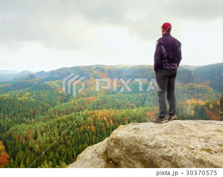 Hiker on rock end above valley, watch over mist Hiker on rock end above valley, watch over mist 30370575