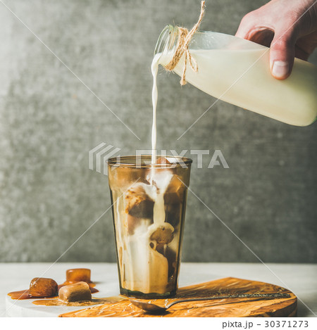 Man's hand pouring milk to cold latte coffee 30371273
