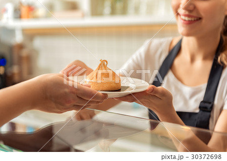 Cheerful saleswoman handing pastry to client 30372698