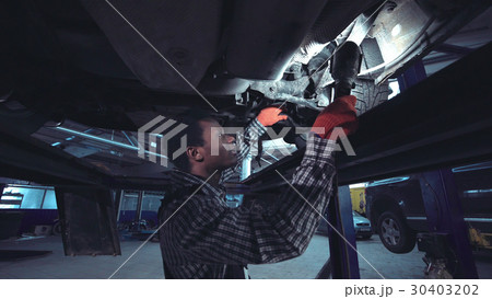 African mechanic working on the underside of a car 30403202