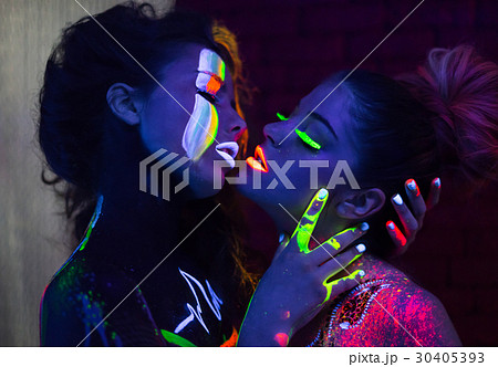 Sexy lesbian fashion models in uv neon light with fluorescent glowing Body  Art make-up hugging kissing. Low key dark image. Soft focus image. Stock  Photo