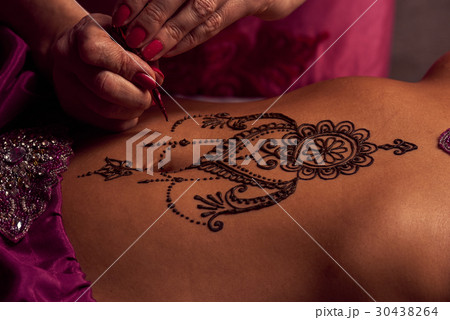 Mehendi artist paints an ornament of henna on an eastern girl Mehendi artist paints an ornament of henna on an eastern girl 30438264