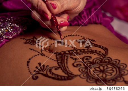 Mehendi artist paints an ornament of henna on an e Mehendi artist paints an ornament of henna on an e 30438266