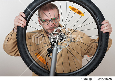 Bearded man puts the front wheel on the bicycle. 30454620