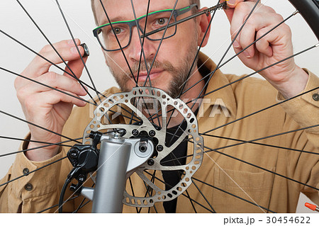 Bearded man screws the front wheel on bicycle. Bearded man screws the front wheel on bicycle. 30454622