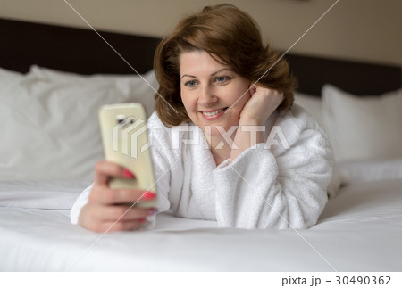 A woman in bathrobe wears telephone in hotel room 30490362