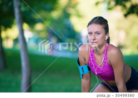 Young female runner is having break and listening Young female runner is having break and listening 30499360