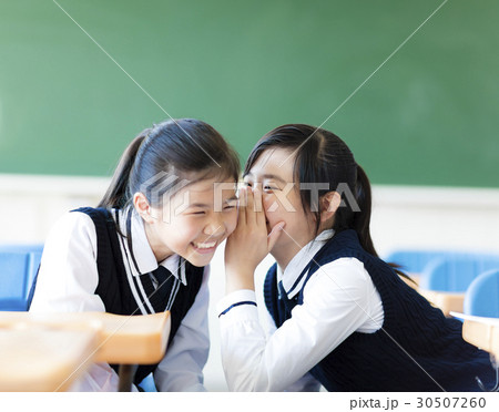 Two teenager girls gossiping in classroom Two teenager girls gossiping in classroom 30507260