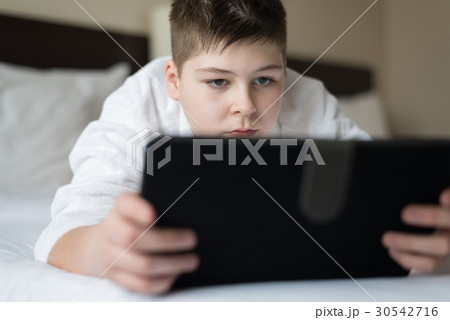 Boy in bathrobe Uses tablet in hotel room 30542716