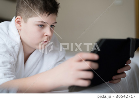 Boy in bathrobe Uses tablet in hotel room 30542717