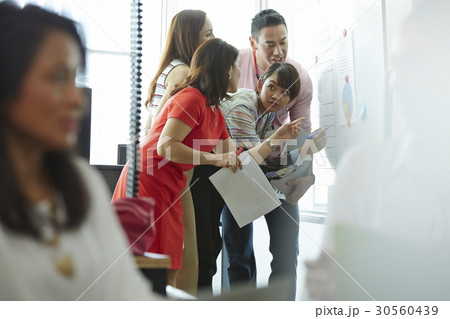Four of five people discussing a chart on a board Four of five people discussing a chart on a board 30560439