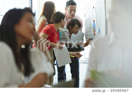 A woman is writing on a board in a group discussion A woman is writing on a board in a group discussion 30560467