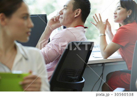A man is talking on phone in office while two women are looking 30560538