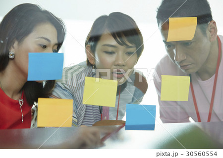 Businesswoman pointing at sticky notes to colleagues in office. 30560554