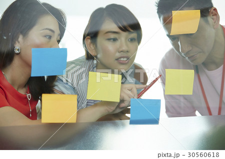 A businesswoman is pointing at sticky notes to colleagues in office A businesswoman is pointing at sticky notes to colleagues in office 30560618