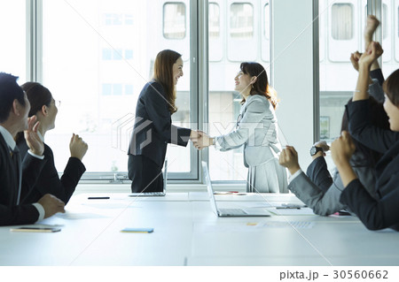 Two businesswomen are shaking hands and some people are cheering. 30560662