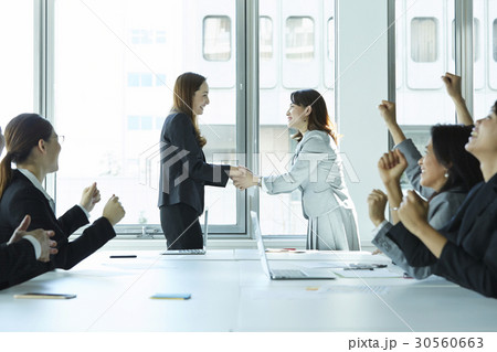 Two businesswomen are shaking hands and some people are cheering. 30560663