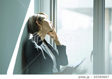 A businesswoman is talking on phone and looking outside in office. A businesswoman is talking on phone and looking outside in office. 30560667