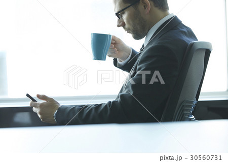 a portrait of a man sitting, drinking and looking at a phone 30560731