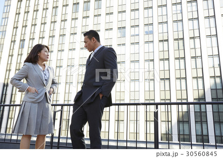 a man and a woman are talking beside a building 30560845
